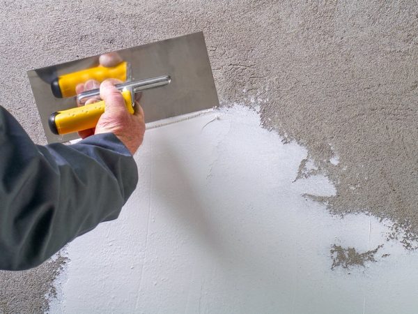 Construction worker - plastering and smoothing concrete wall with white stucco by a steel trowel - spatula aligns